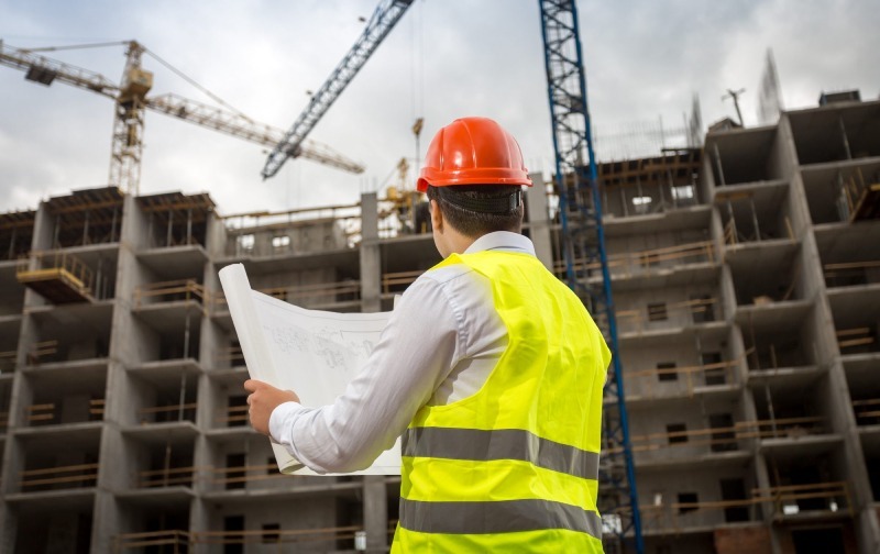 Giám Sát Công Trình Hiệu Quả: Hướng Dẫn Từ A-Z Cho Người Xây Nhà Kỹ sư đội mũ đỏ cầm bản vẽ giám sát công trình