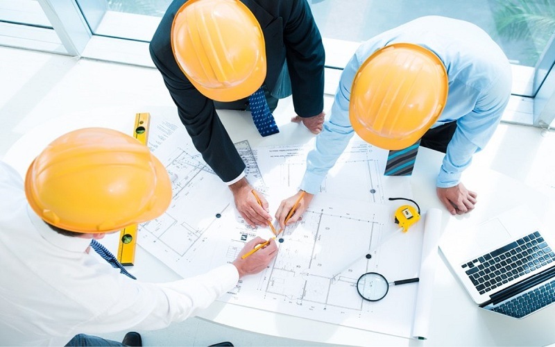 Tư Vấn Xây Nhà Lần Đầu: Tránh 5 Sai Lầm Phổ Biến Dễ Mắc Nhất Nhóm kỹ sư đội mũ bảo hộ đang tư vấn xây nhà lần đàu thảo luận bản vẽ xây dựng trên bàn