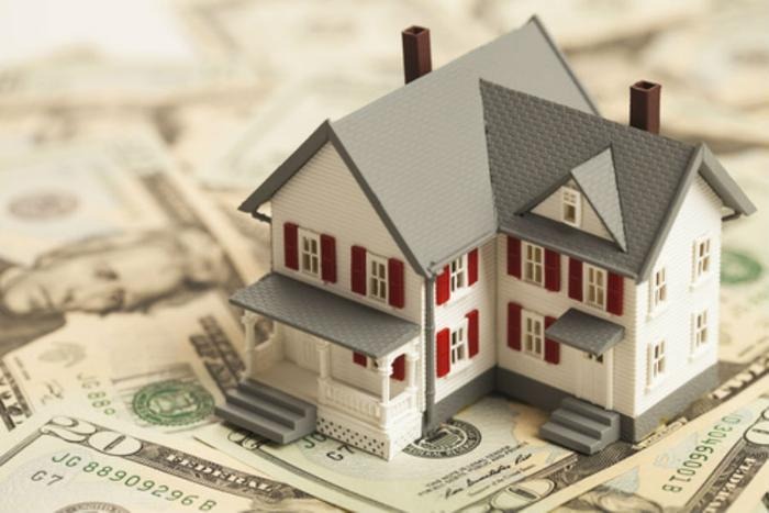 Xây Nhà Cần Chuẩn Bị Gì? 6 Bước Quan Trọng Giúp Bạn Không Vỡ Kế Hoạch Mô hình ngôi nhà đặt trên tiền mặt tượng trưng cho chi phí xây nhà cần chuẩn bị gì