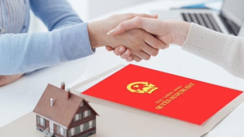 Hai người bắt tay bên cạnh sổ đỏ và mô hình nhà, minh họa cho thủ tục xin phép xây dựng nhà ở.